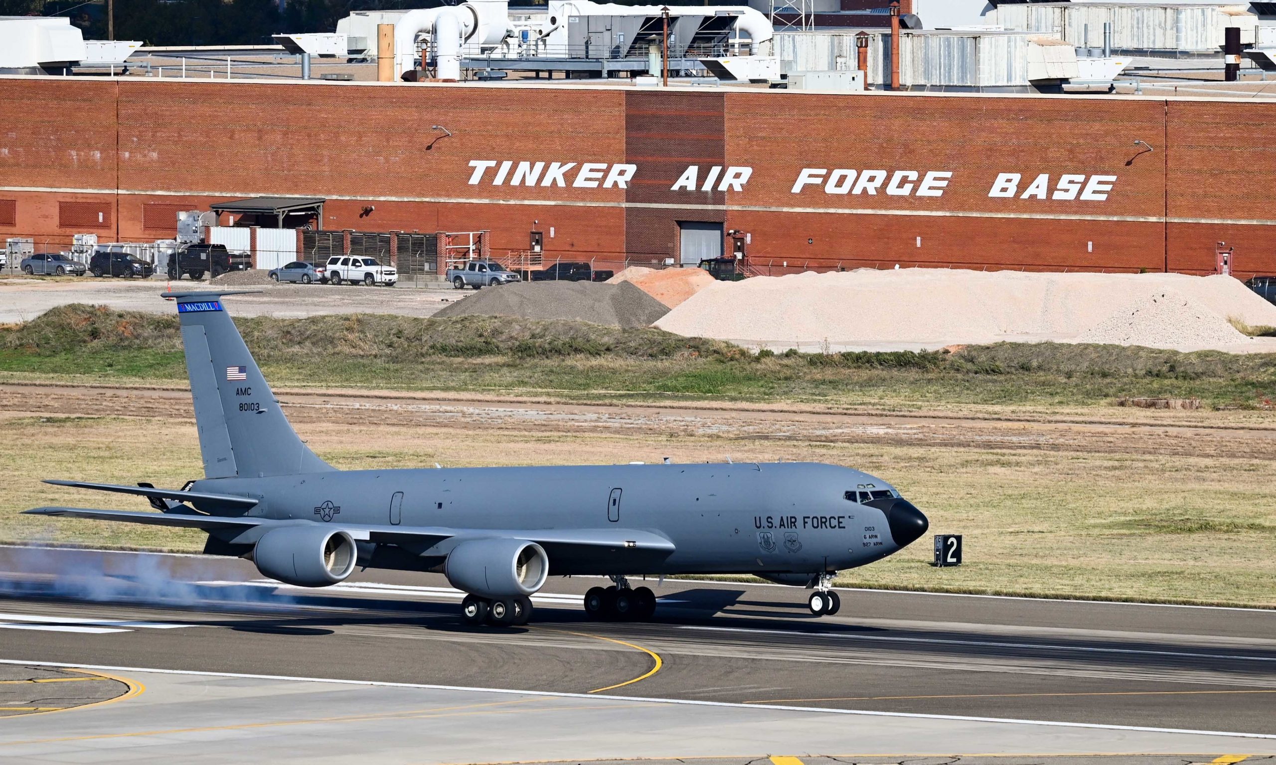 A U.S. airforce airplane taking of of a runway with a sign reading "Tinker Air Force Base" behind it on a brick building