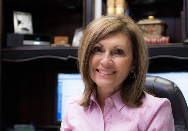 a woman smiling with brown hair and a pink button up blouse